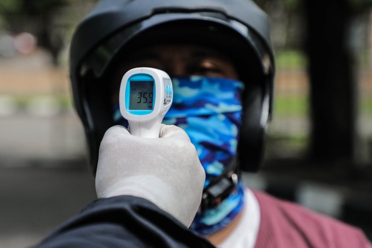 Un gardien de sécurité vérifie la température corporelle d'un motocycliste à titre préventif.